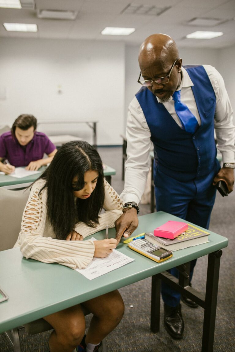 Educator assisting student during an exam in a classroom setting, emphasizing support in education.