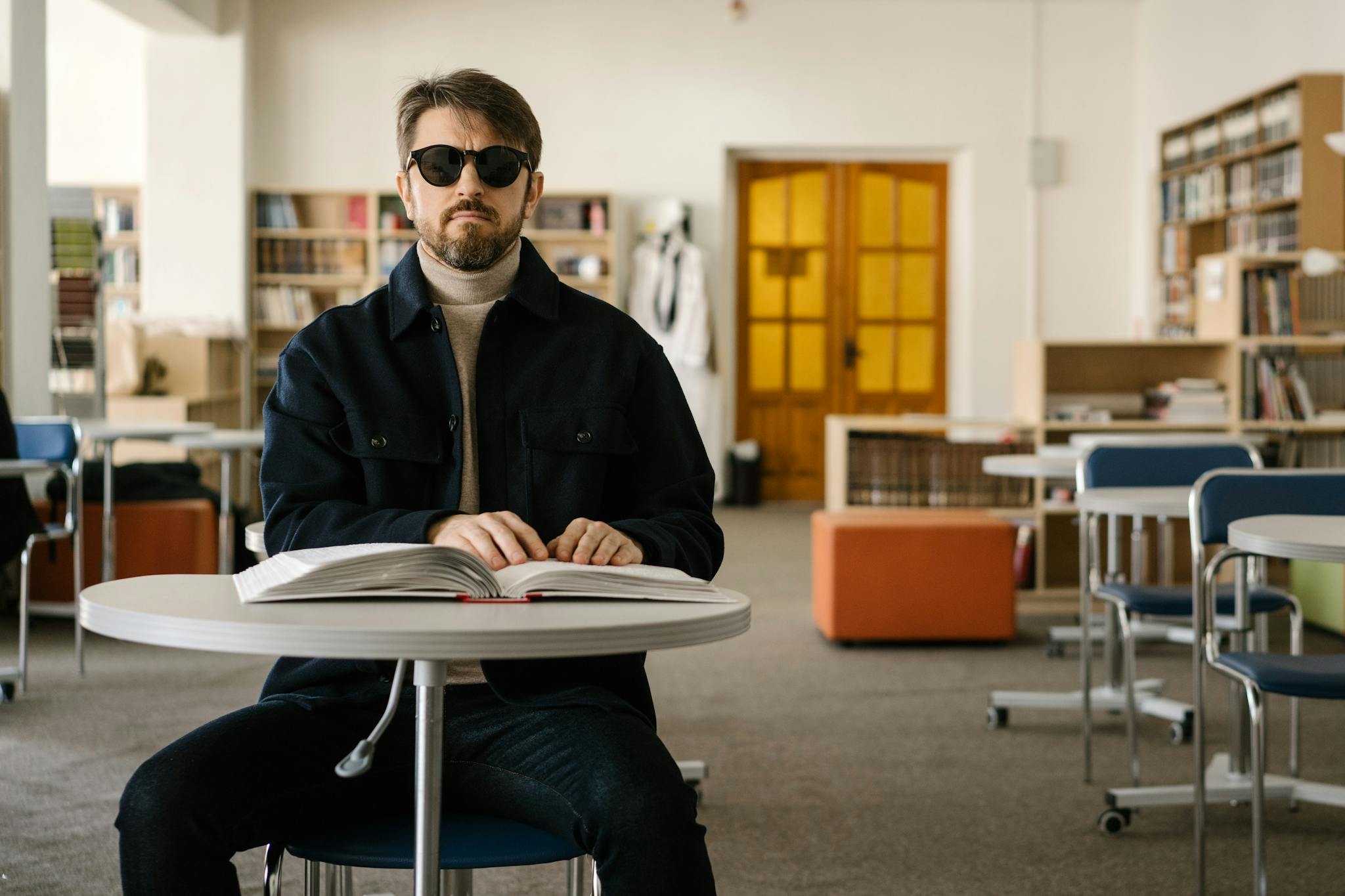 Visually impaired man reads Braille book in an indoor library setting.