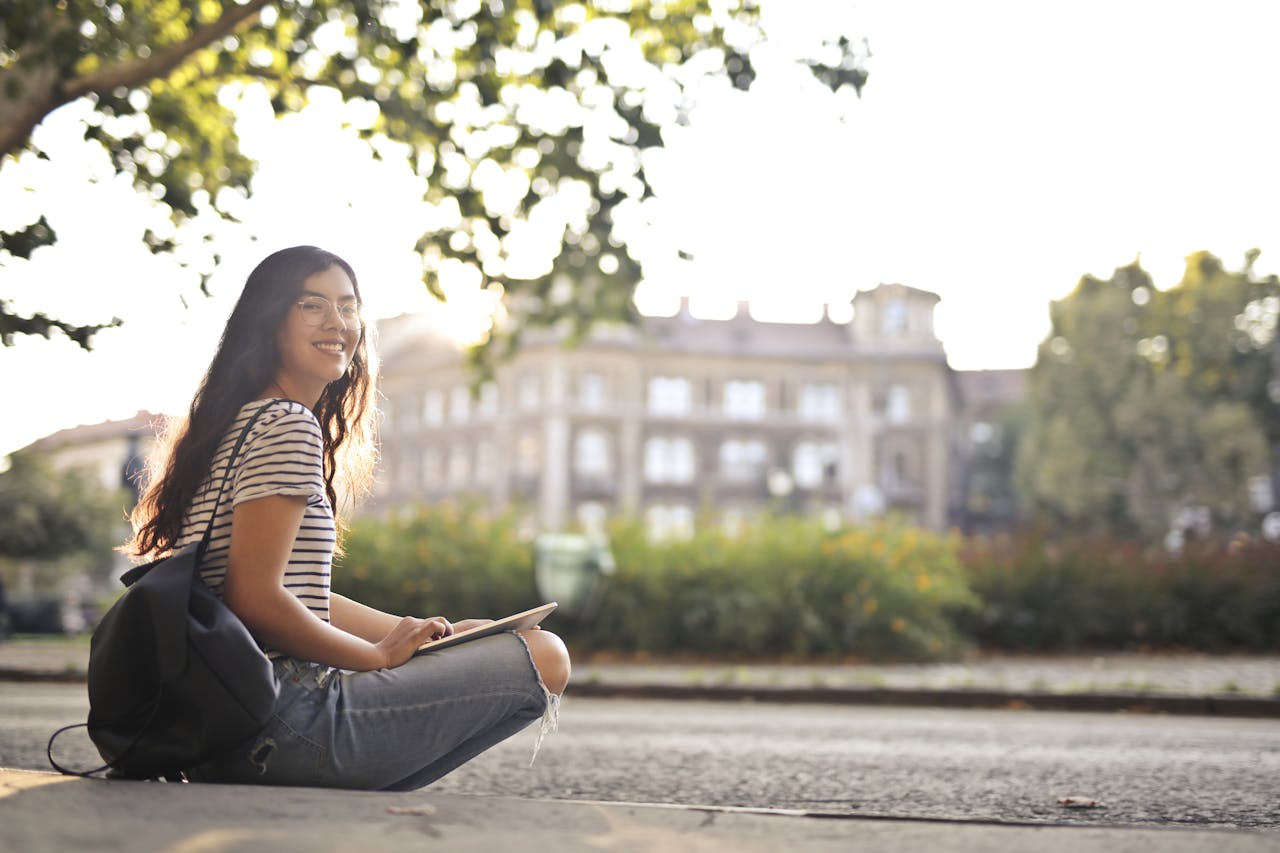 Happy woman in striped shirt sitting outside on sunny day with a tablet.