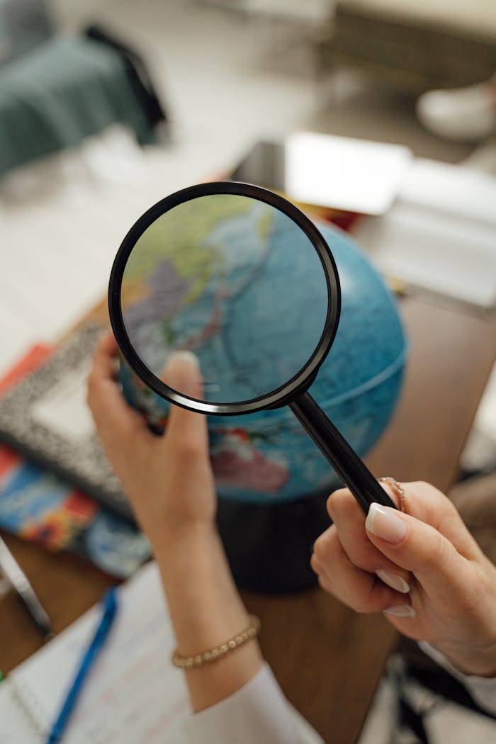 Hands holding a magnifying glass over a globe, symbolizing exploration and research.